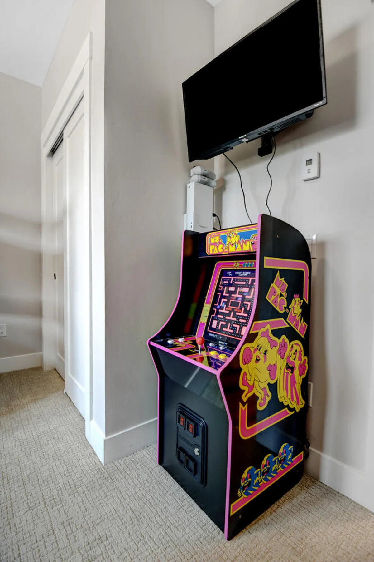 A dedicated gaming nook features an arcade cabinet and a nearby television, set against a cozy carpeted backdrop. The space feels both nostalgic and playful, perfect for competitive fun and relaxing downtime.