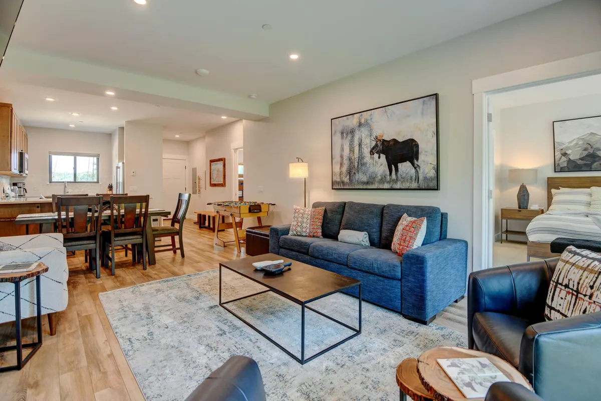 A spacious, comfortable living room featuring a sofa with decorative cushions, an eye-catching moose painting, and a dining table with chairs—all arranged in an open-concept layout perfect for gatherings.
