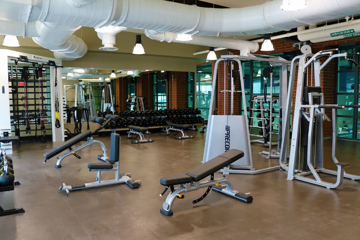 A bright fitness center filled with modern workout equipment, including weightlifting benches, dumbbells, and exercise machines. The energetic setting suggests opportunities for both individual fitness and group workouts.