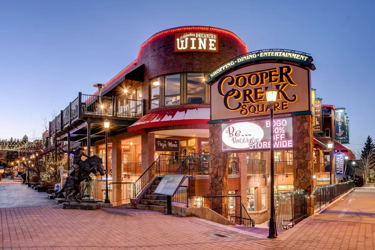 This image features the Cooper Creek Square sign alongside a lively wine shop entrance and outdoor seating area. Festive seasonal decorations and people gathered for evening entertainment set a vibrant and welcoming scene, capturing the essence of downtown Winter Park's social atmosphere.