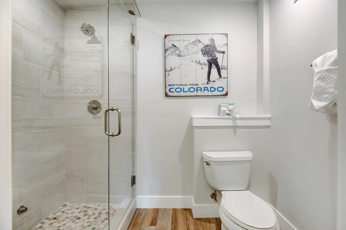A modern bathroom featuring a glass shower enclosure, neutral color palette, and a vintage Colorado poster. The design evokes relaxation and luxury, perfect for spa-like self-care routines.