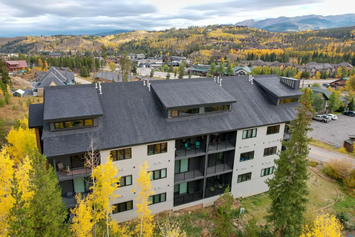 An exterior view highlighting modern architecture set against stunning autumn foliage and distant Rocky Mountains. The scene invites viewers outdoors and hints at hiking, wildlife viewing, and evening relaxation on the balcony with sweeping mountain vistas.