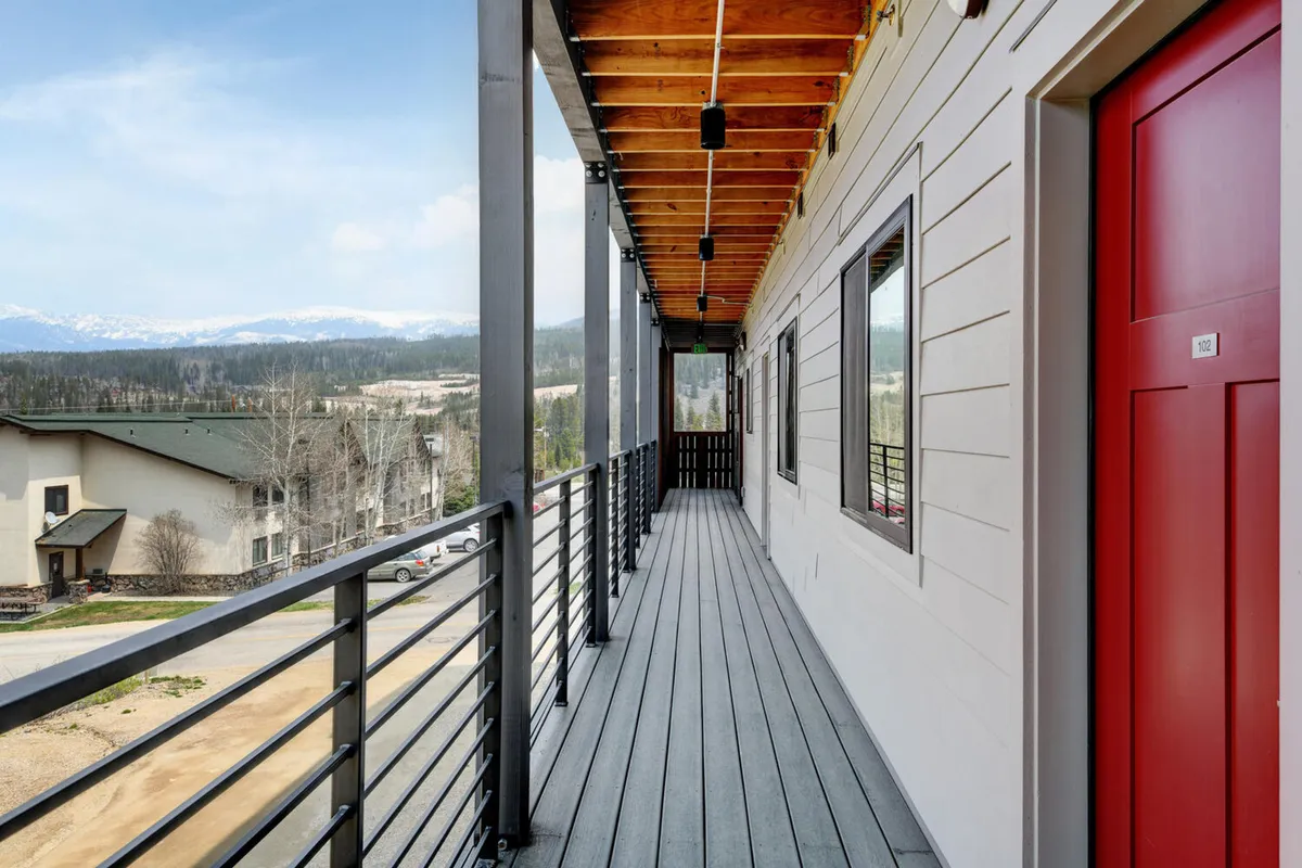 A tranquil exterior shot featuring a red door, a balcony with railing, and expansive mountain views in the background. The mood is peaceful, suggesting moments spent unwinding after adventure-filled days while savoring the mountain air.